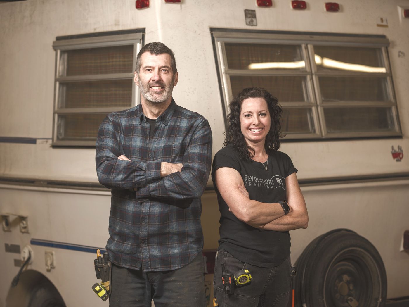 Stu and Maegan in front of a vintage trailer inside their shop.