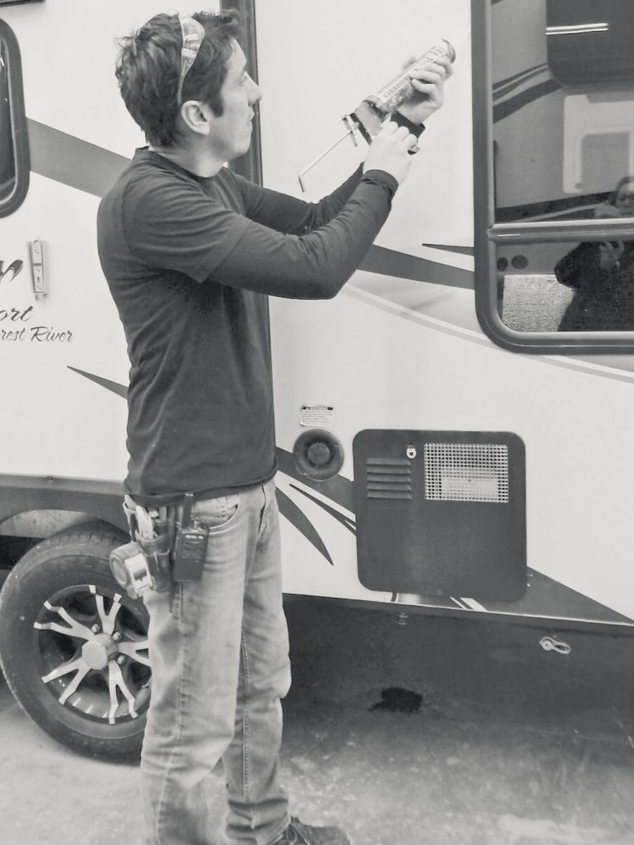A technician sealing the exterior of a travel trailer.